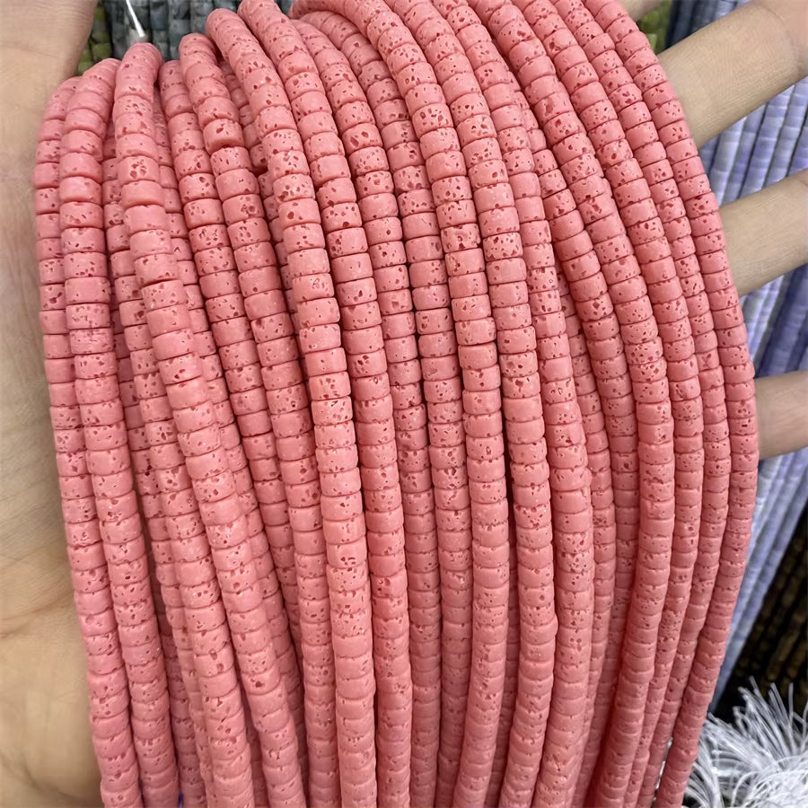 A close-up of a hand holding a bundle of coral pink volcanic rock beads, showing the detailed porous surface of each bead.