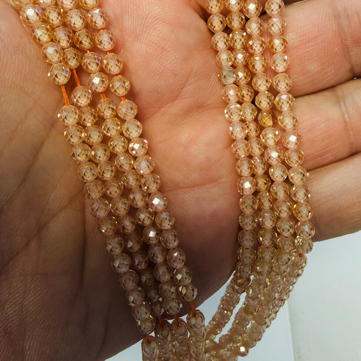 Faceted round beads in a warm peachy-brown color threaded on strings, held in a person's hand to show the strand count and texture.