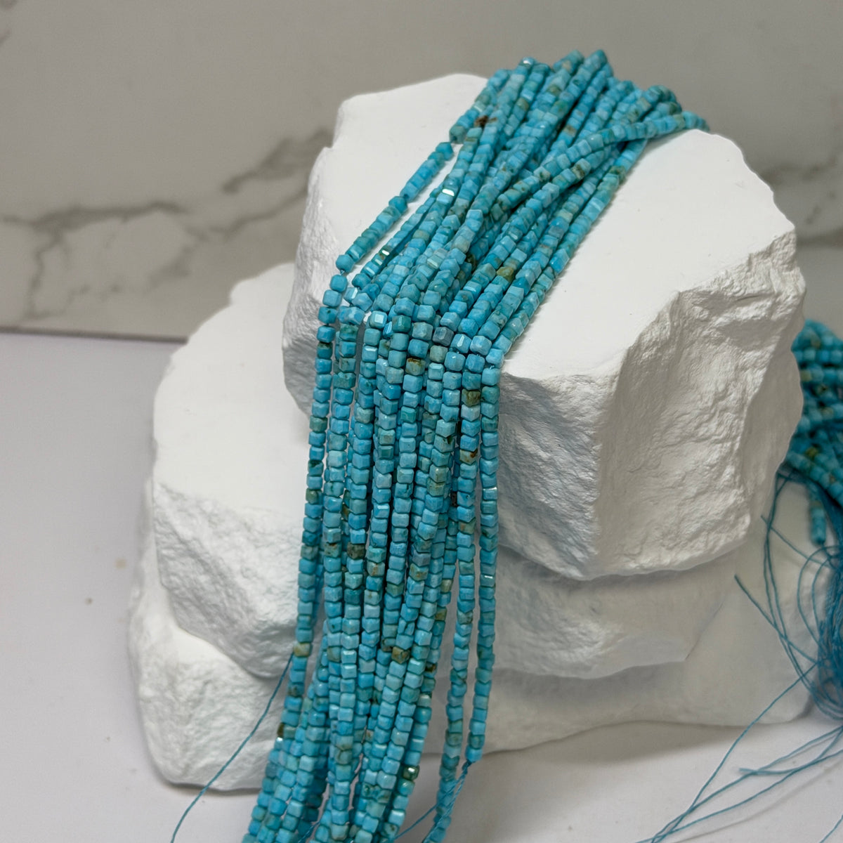 Multiple strands of faceted turquoise beads draped over a white display block, photographed indoors with a blurred background.