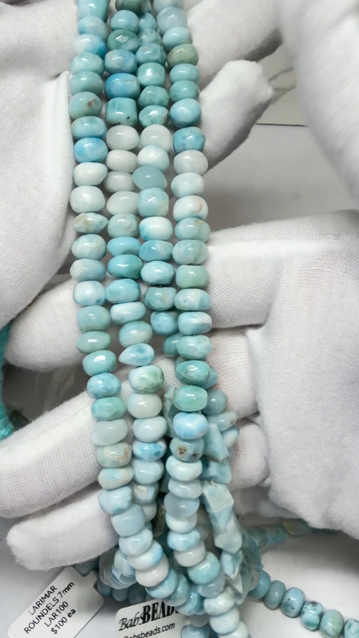 Larimar Roundel Bead Strands Draped over white gloved hands