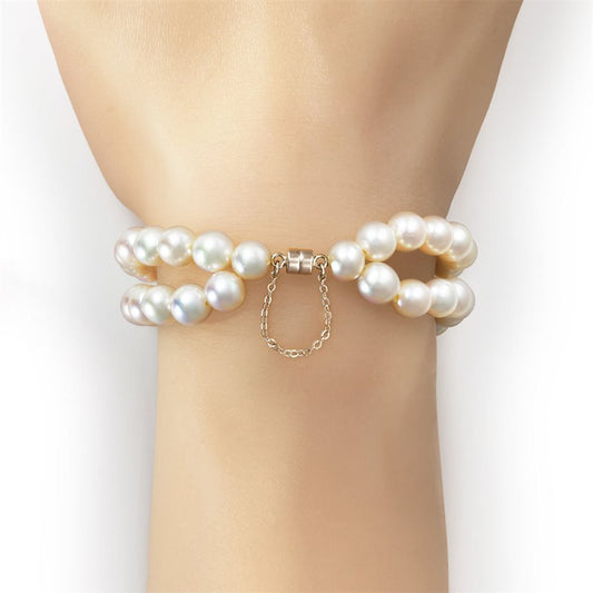 A double-strand pearl bracelet with a gold clasp and dangling chain, shown worn on a model's wrist against a clean white background.