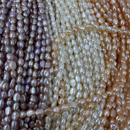 Close-up of strands of irregular baroque pearls in multiple colors, including lavender, cream, and peach, arranged vertically.