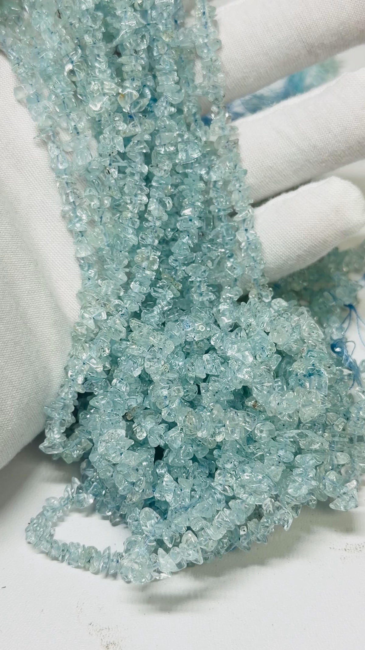 Strands of aquamarine tumble chips on a hand with a white glove