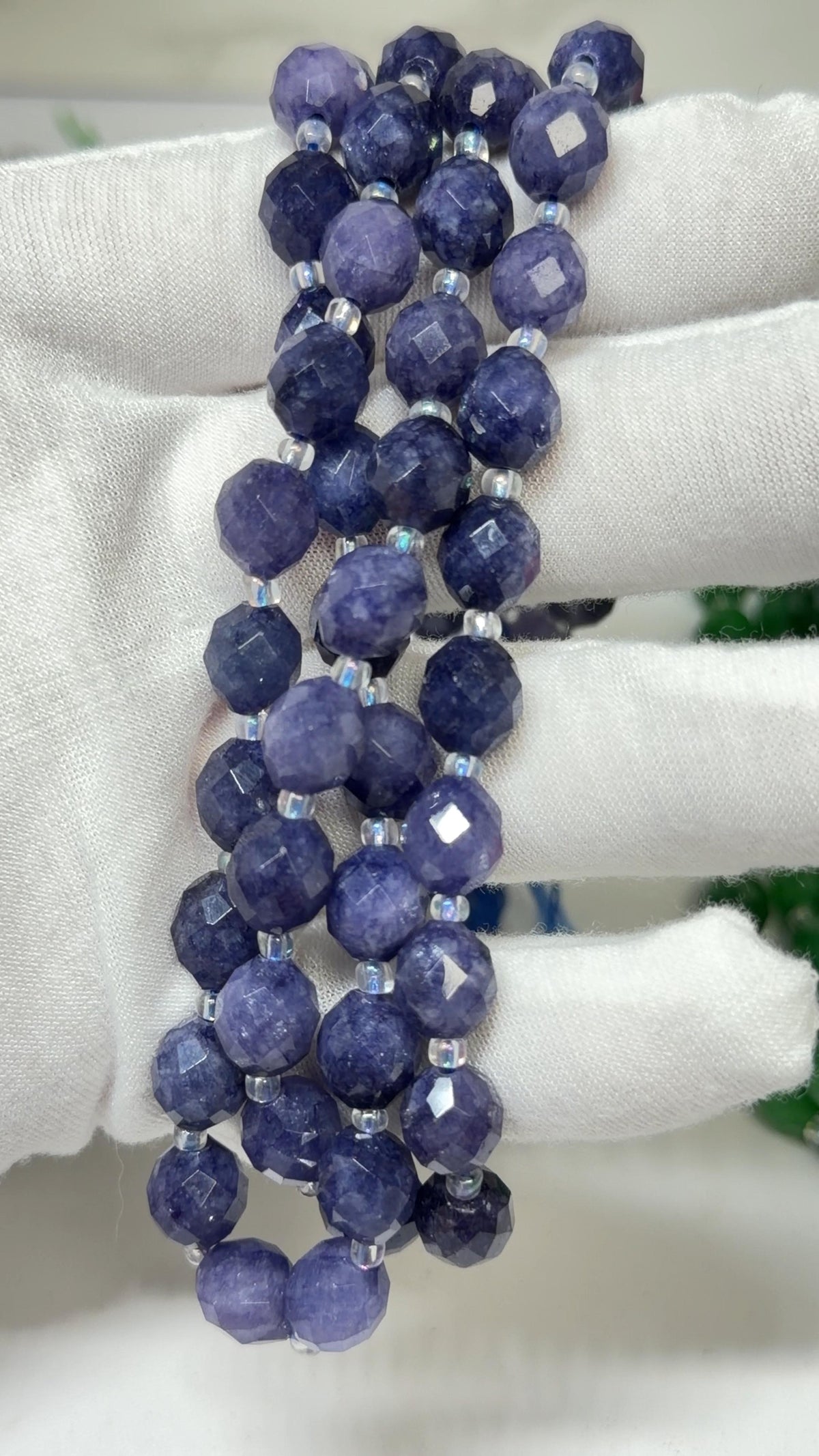 A close-up of a beaded strand made of round faceted beads in blue tones, held in a white gloved hand.