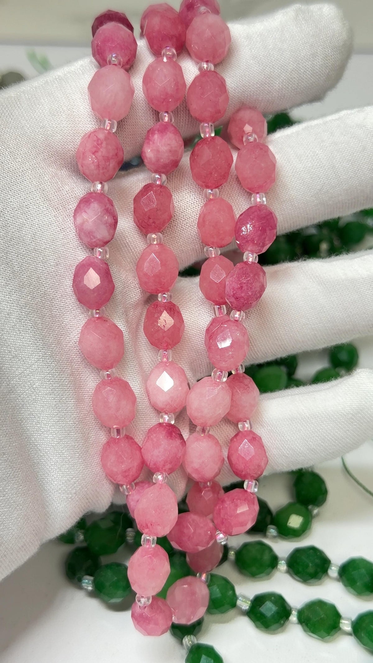 A close-up of a beaded strand made of round faceted beads in pink tones, held in a white gloved hand.