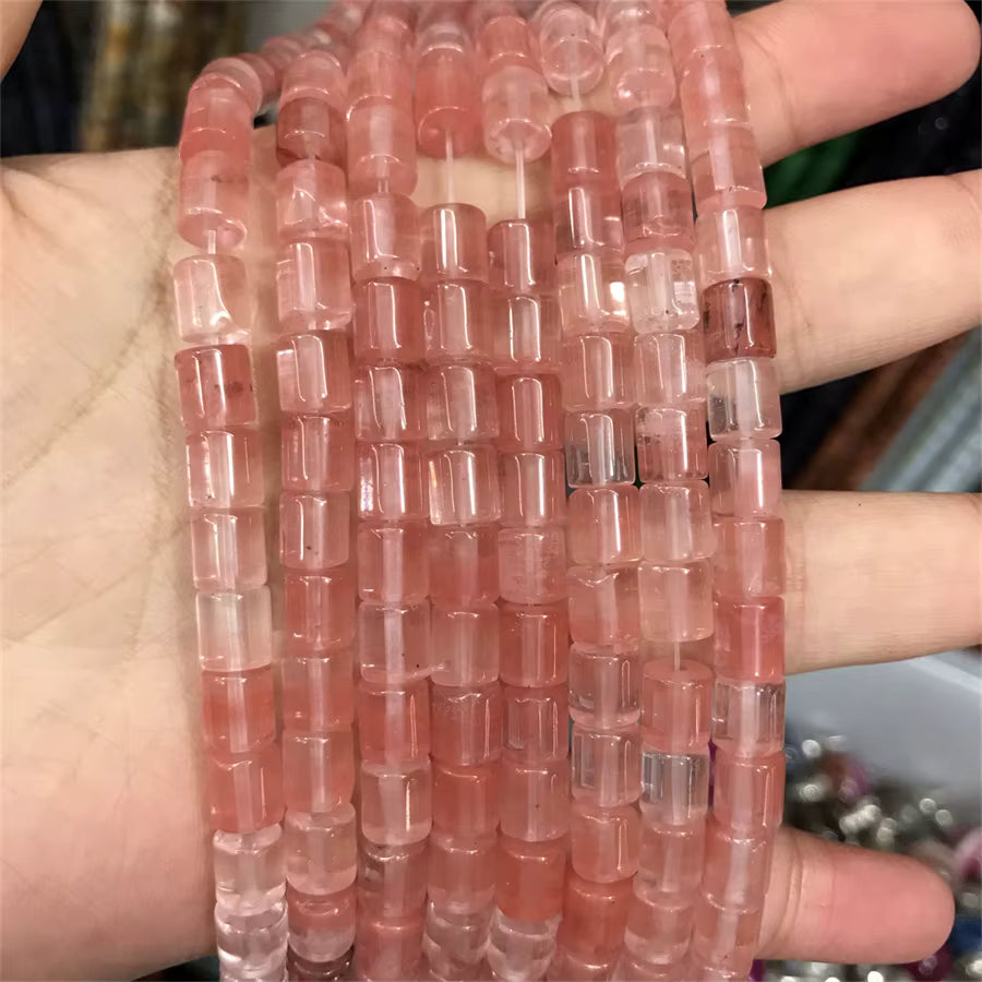 A hand holding multiple strands of pink translucent cylindrical beads, likely for jewelry making.