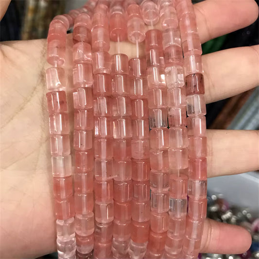 A hand holding multiple strands of pink translucent cylindrical beads, likely for jewelry making.