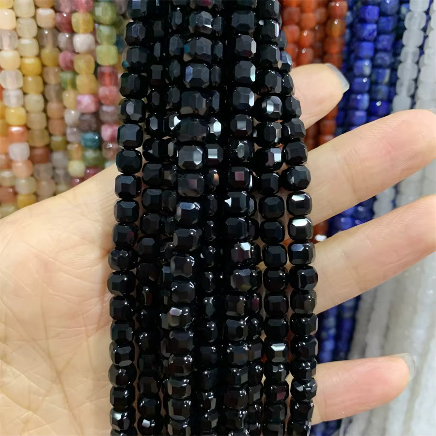 Faceted black beads strung on cords, held in a hand against a background of other colorful bead strands.