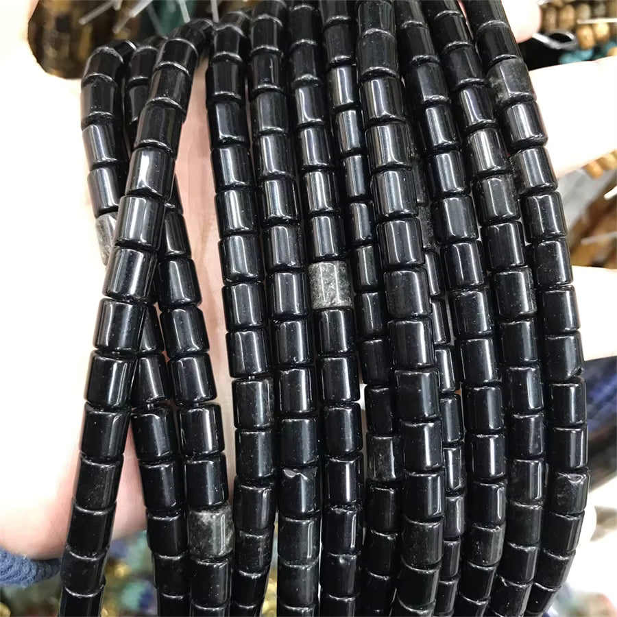 Multiple strands of glossy black cylindrical beads with a beaded tube pattern, held in a hand against a blurred background.