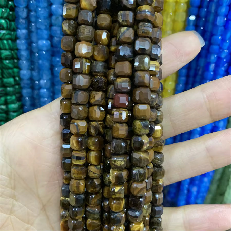 Faceted brown and gold tiger's eye beads strung on cords, held in a person's hand with colorful blue, green, and yellow bead strands blurred in the background.