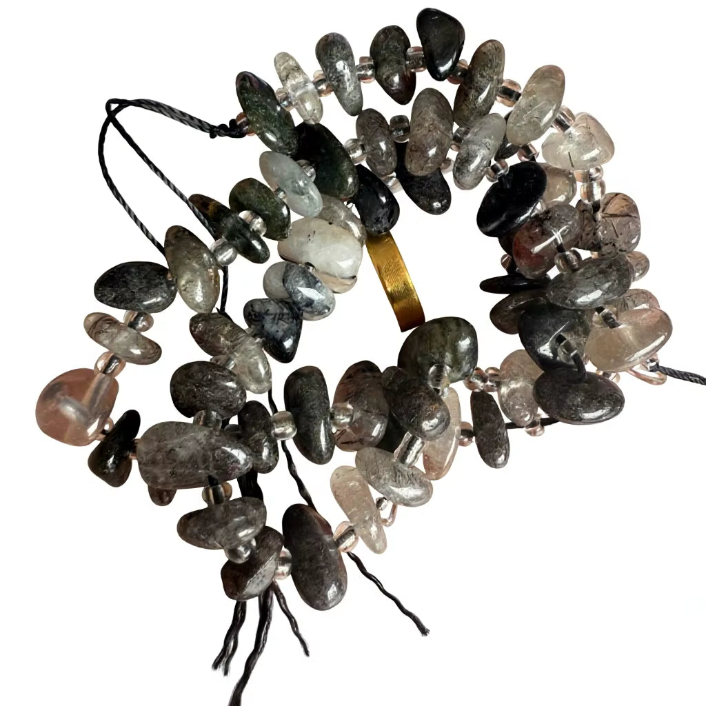 A coiled strand of polished tumbled stone chips in mixed earthy tones including gray, black, brown, beige, and translucent white, strung on black cords with a small gold spacer visible.