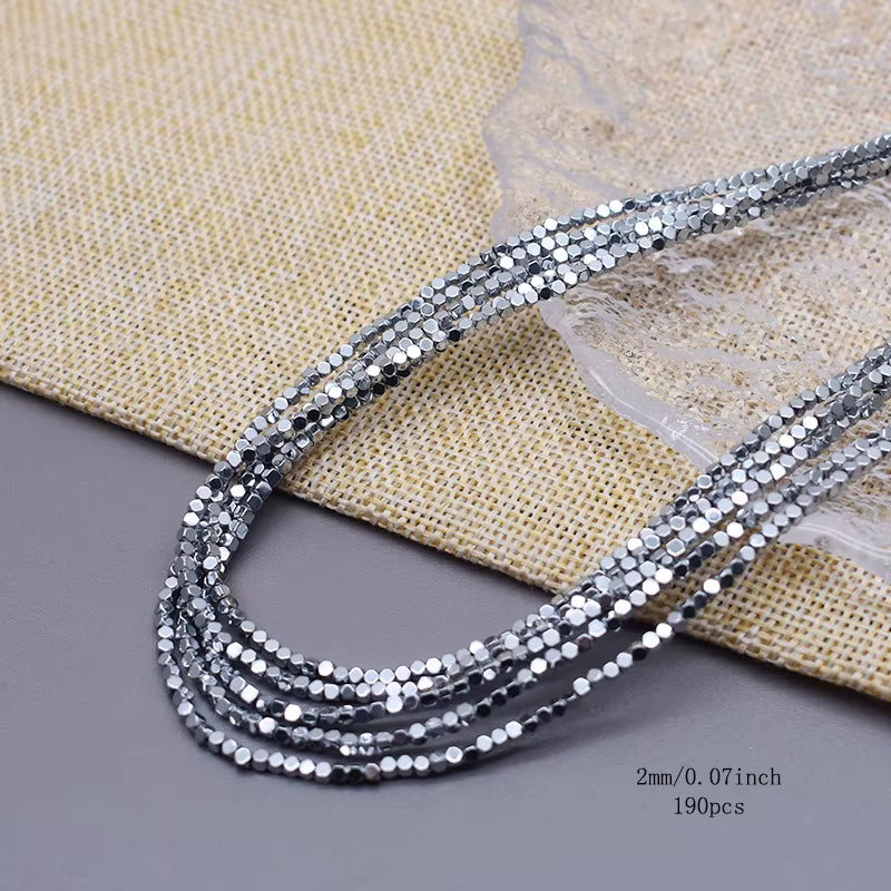 Five strands of silver faceted round beads, 2mm (0.07 inches) in diameter, laid out on a beige woven mat and gray surface.