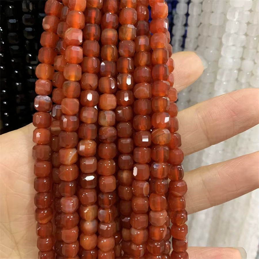 Faceted cube beads in a warm reddish-orange marbled pattern, strung on cords and held in a hand to show scale.