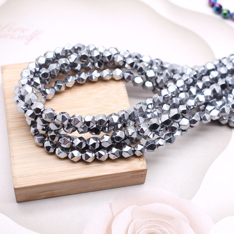 Faceted silver beads arranged in a loop on a small wooden block, photographed on a soft white background with decorative floral elements.