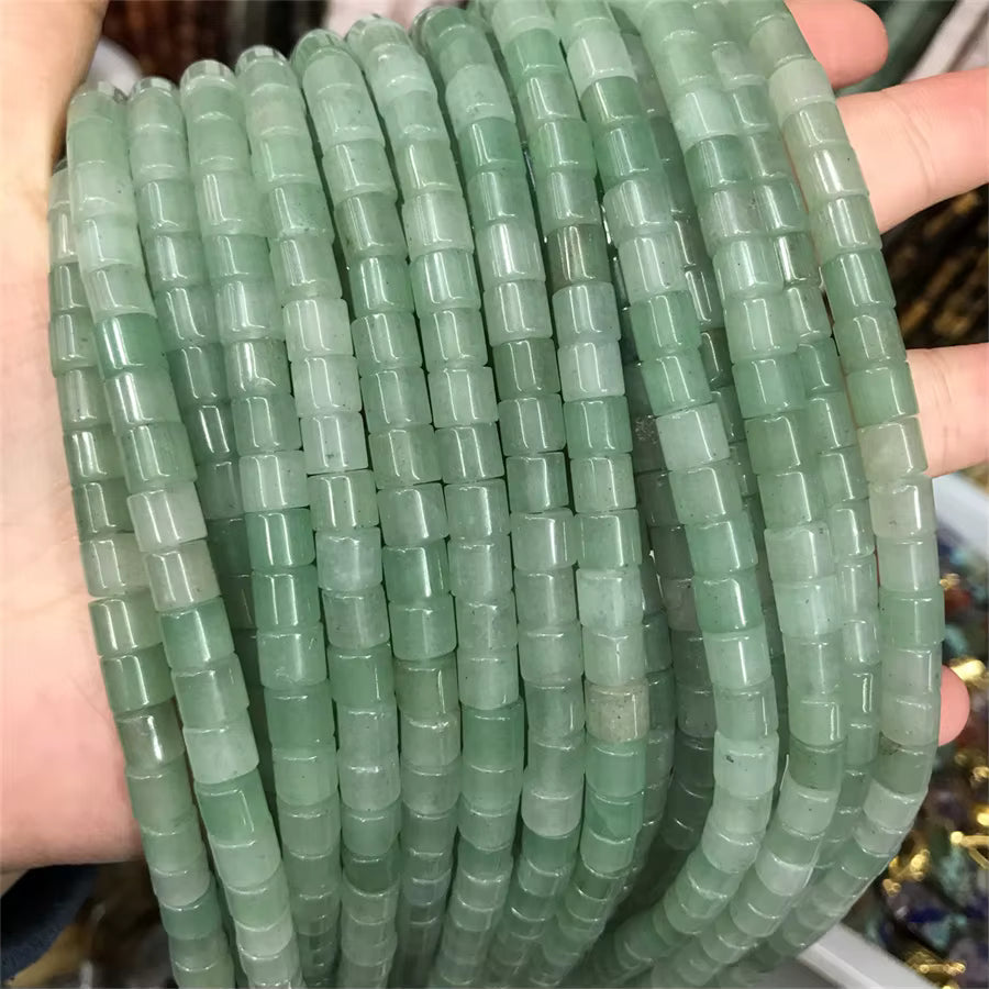 A close-up of multiple strands of cylindrical green beads held in a person's hand. The beads are translucent and have a light green to mint green color, arranged in parallel rows.