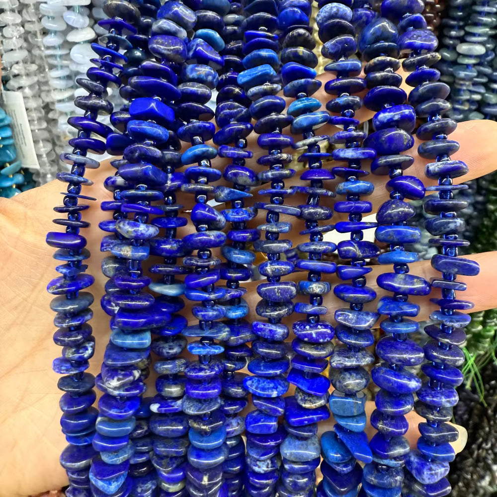 Multiple strands of polished cobalt blue lapis lazuli stone chips held in a person's hand, showing natural white veining and rounded disc-shaped beads.
