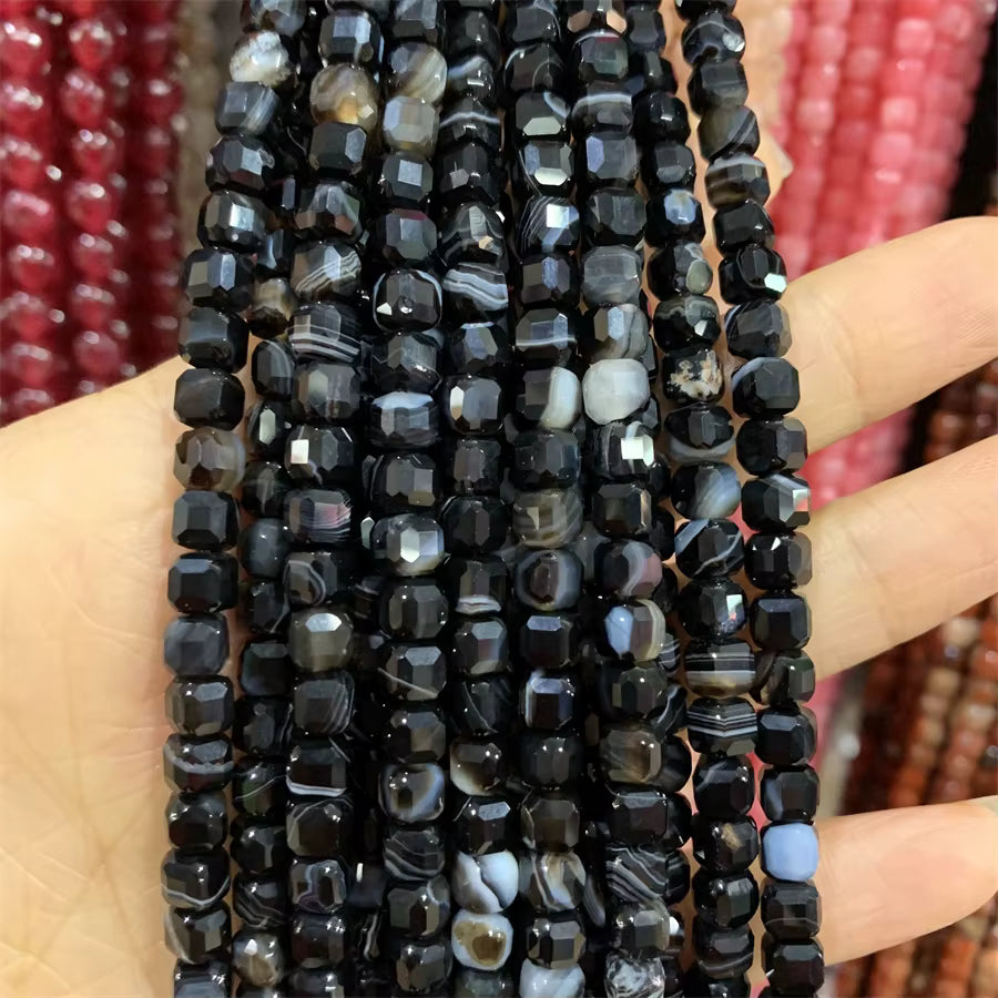 Faceted black agate beads strung on multiple strands, held in a person's hand against a blurred background of red and brown beads.