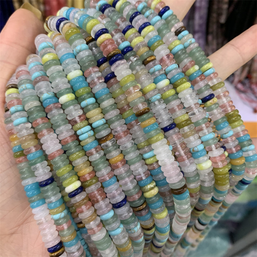 Assorted strands of 2x6mm spacer gemstone beads laid out over a hand