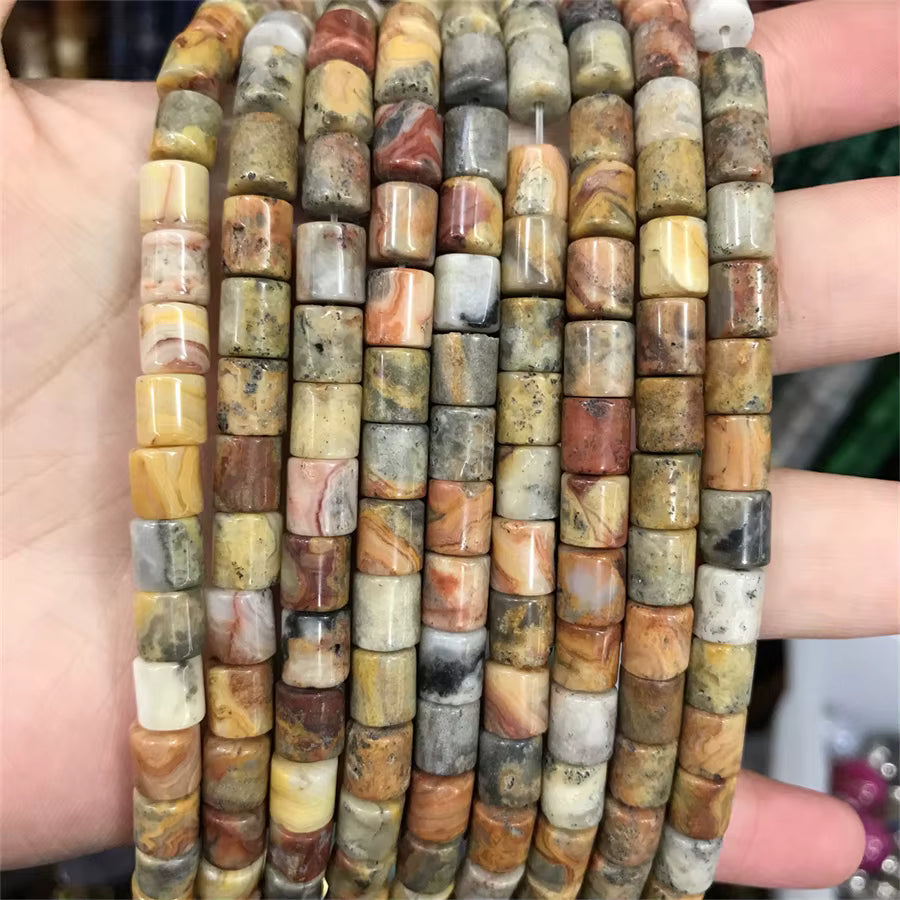 Multiple strands of cylindrical stone beads with natural marbled patterns in earthy tones of brown, beige, gray, and cream, held in a person's hand.