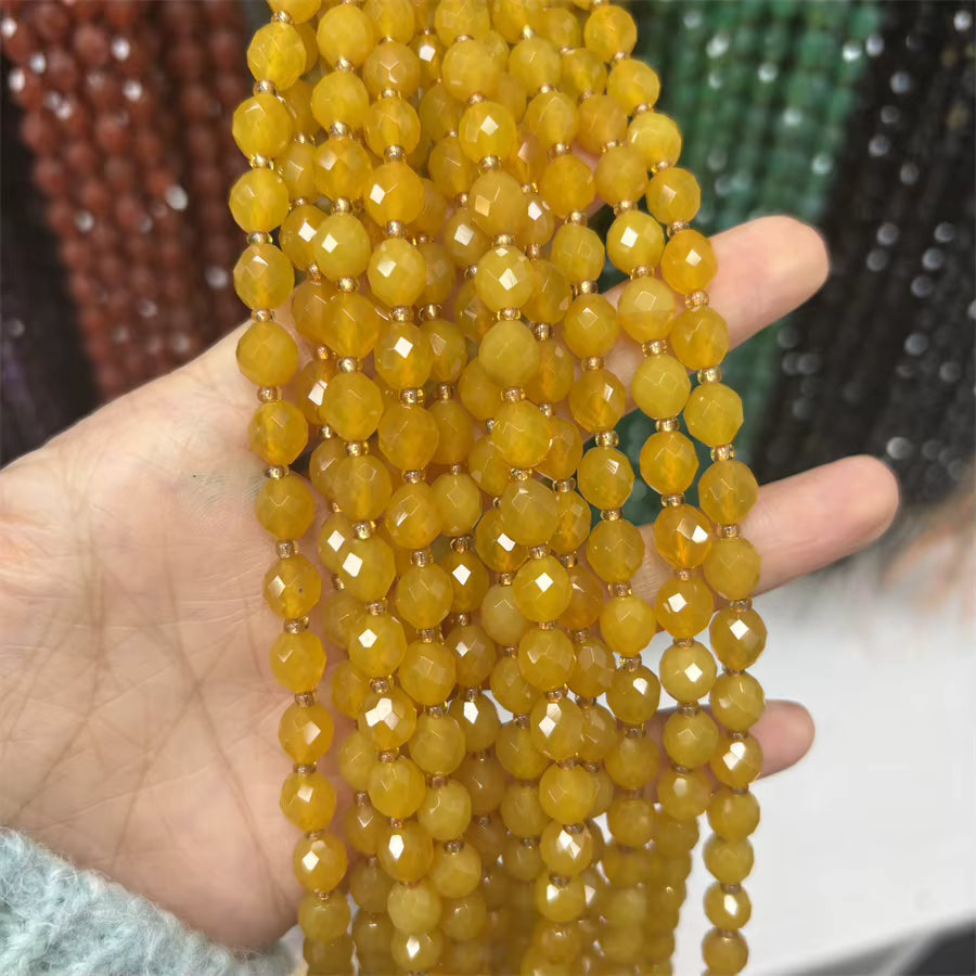 A hand holding multiple strands of faceted yellow beads, with other colorful bead strands blurred in the background.
