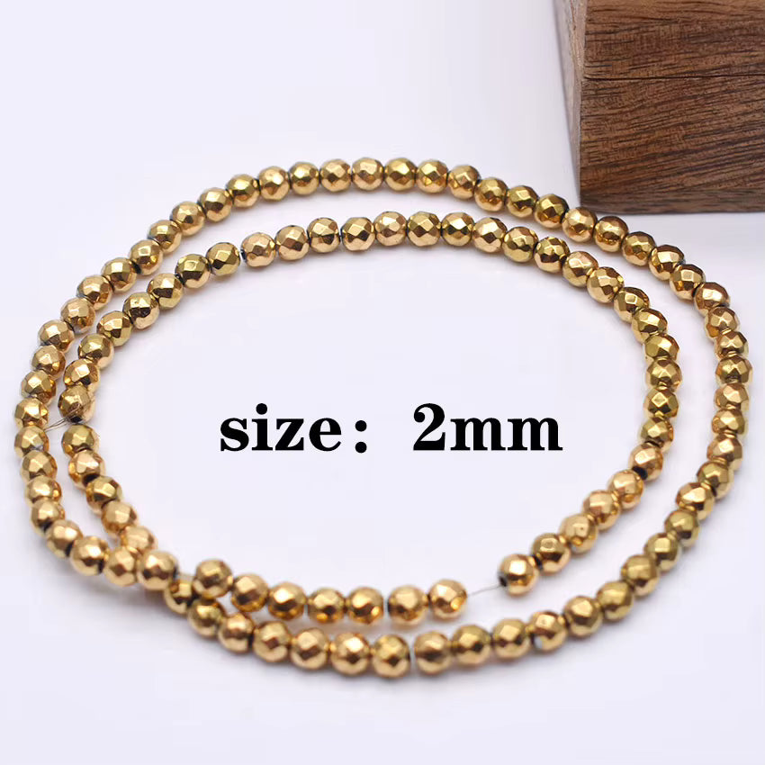 Two strands of small metallic gold faceted beads coiled on a white background, with black text reading 'size: 2mm' and a brown wood block in the top right corner.