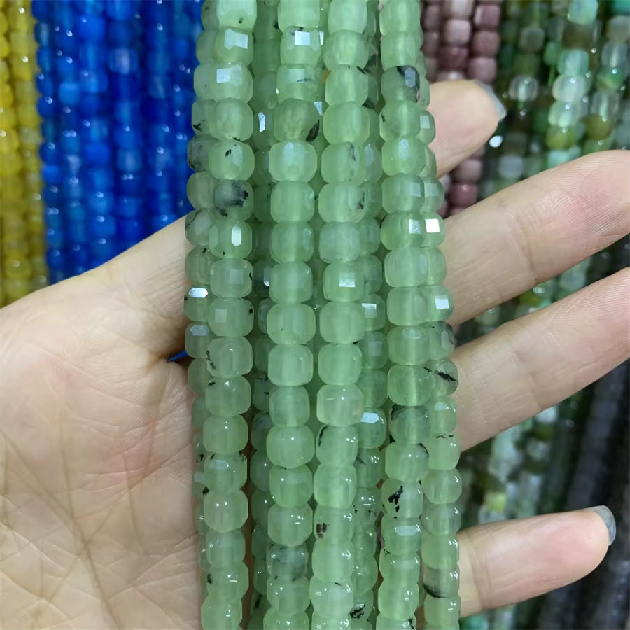 A hand holding several strands of faceted light green beads, with other colorful bead strands blurred in the background.
