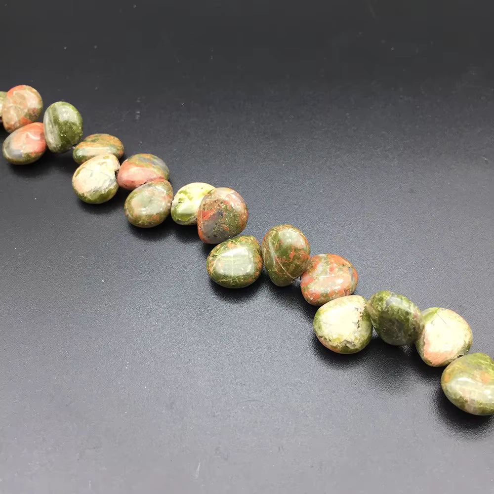 A diagonal strand of polished stone beads with mottled green, orange, and cream colors, displayed on a dark gray background.