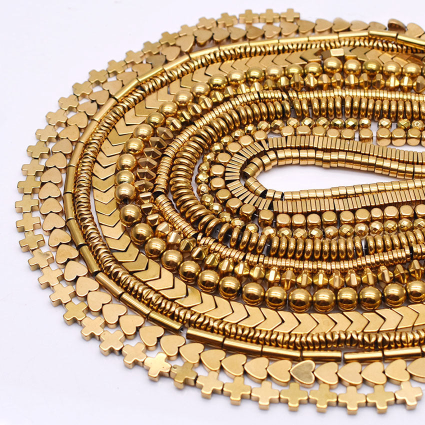 Multiple strands of gold colored hematite in different shapes on a white background 