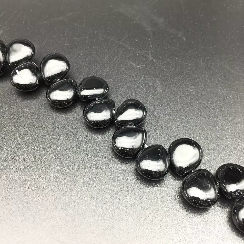 A close-up of glossy black pebble-shaped beads arranged diagonally on a textured gray background.