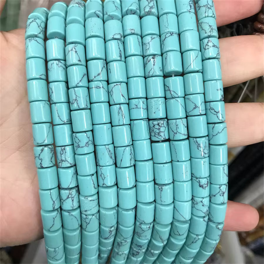 A hand holding multiple strands of cylindrical turquoise beads with natural stone matrix veining, shown close-up against the person's fingers.