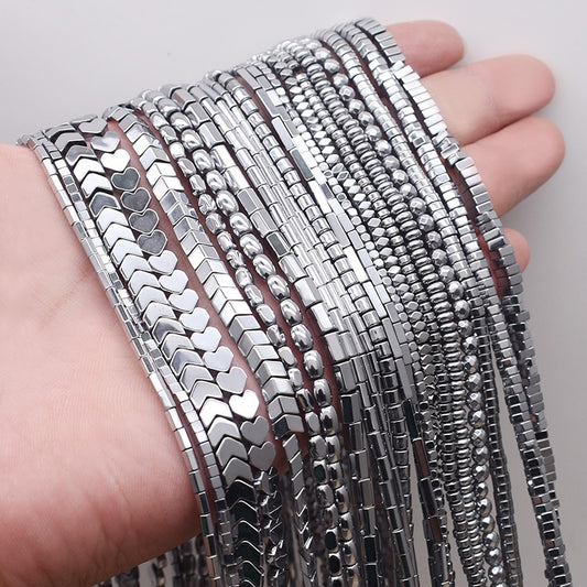 A hand holding different shapes of silver coated hematite beads on a white background 