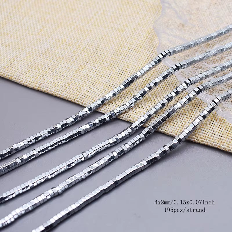 Five strands of silver hex hematite beads  on a gray surface with a beige woven fabric backdrop.  text in the bottom right specifies 4x2mm/0.