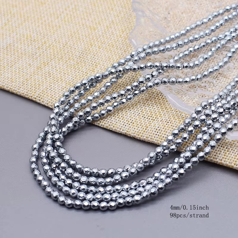 Five strands of shiny metallic silver faceted beads, shown in a coiled arrangement on a textured beige fabric and gray surface. Text in the bottom right corner reads '4mm/0.