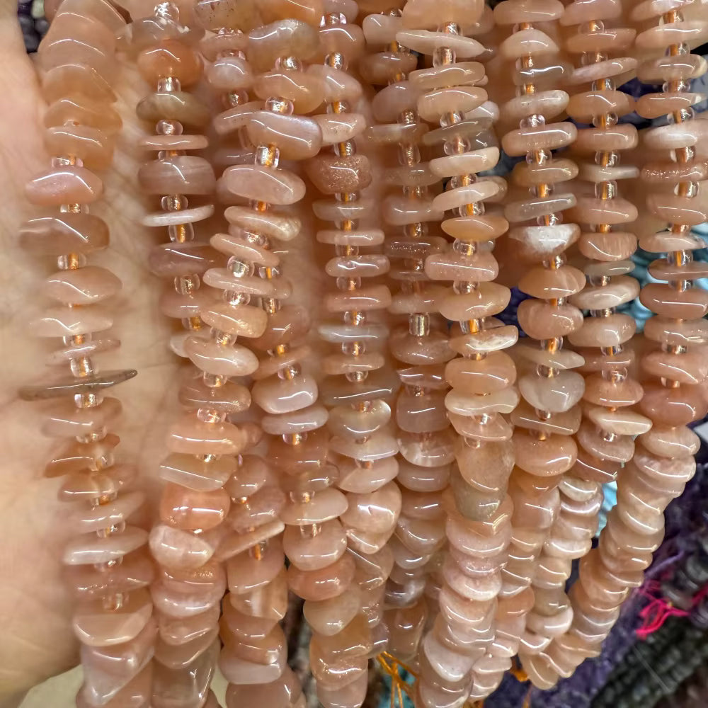 Multiple strands of polished cat's eye stone chip beads in a peachy pinkish-brown hue, held in a hand.