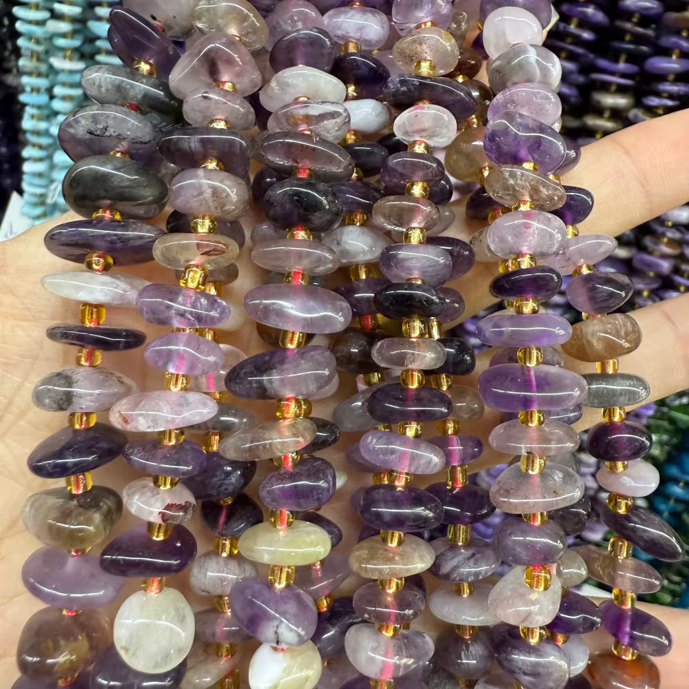 Multiple strands of polished tumbled gemstone beads in shades of purple, lavender, gray, and white, separated by small gold spacer beads, held in a hand.