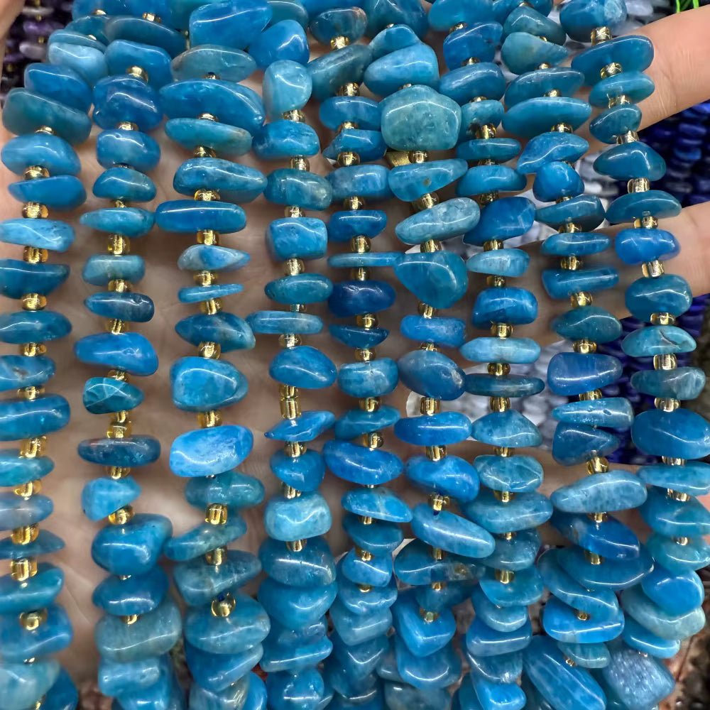 Multiple strands of polished blue stone beads, likely tumbled lapis lazuli or similar turquoise-blue stone chips, threaded with small gold spacer beads, held up against a skin background.