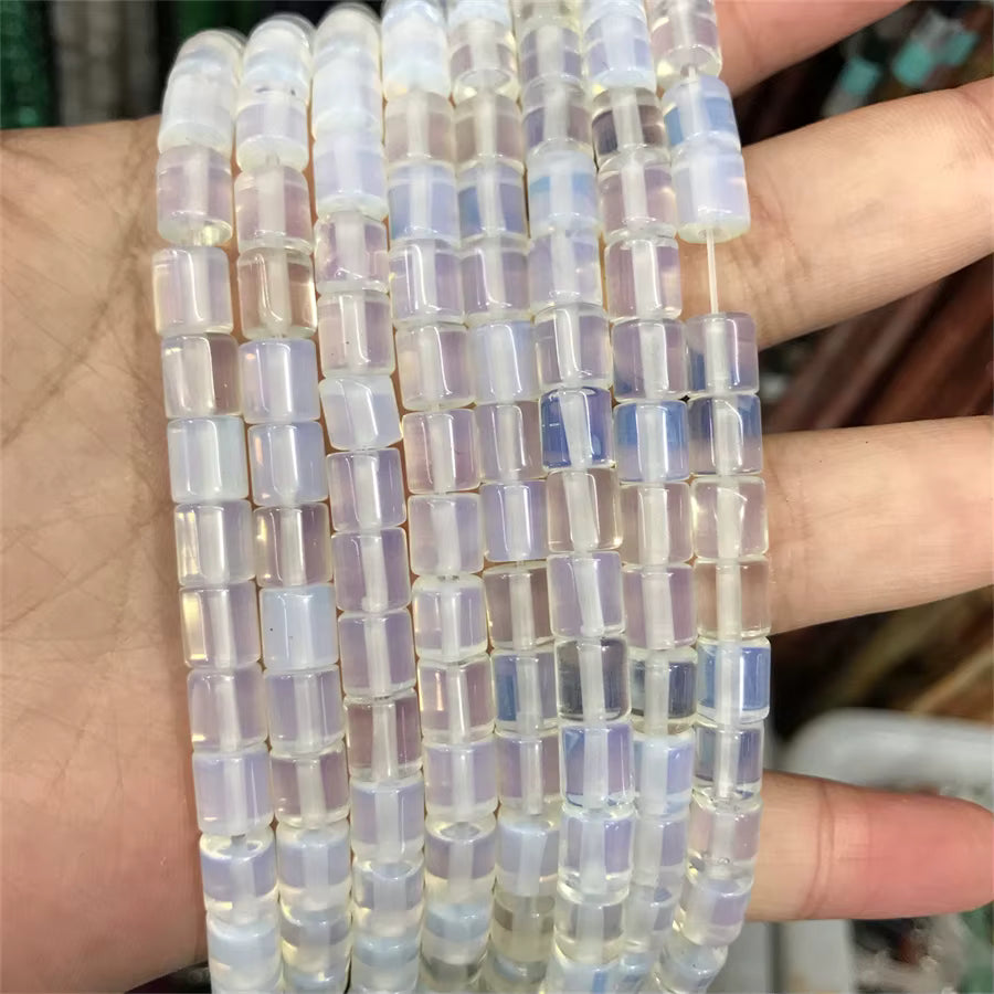 Multiple strands of cylindrical iridescent beads held in a person's hand. The beads have a milky white base with a soft pastel rainbow sheen, showing hues of lavender, blue, and green.