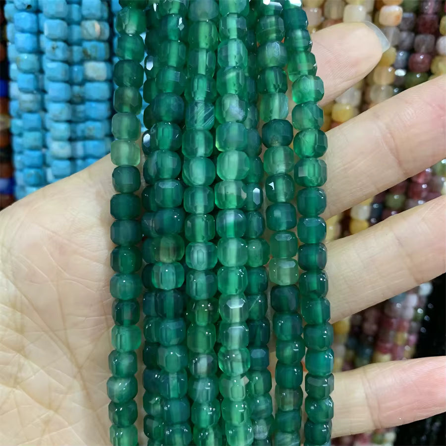 A hand holding several strands of faceted green agate beads, with other colorful bead strands blurred in the background.
