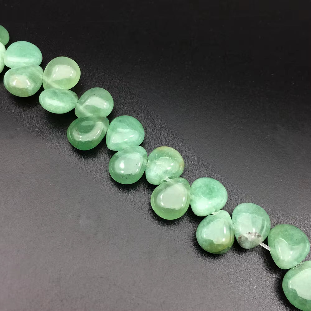 A strand of polished green gemstone beads arranged diagonally on a dark, matte background.