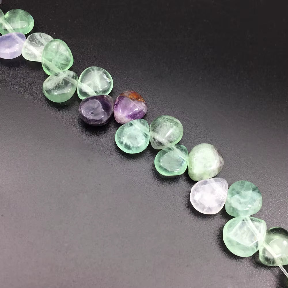 A strand of polished tumbled gemstone beads in light green, lavender purple, and pale pink, arranged diagonally on a dark gray background.