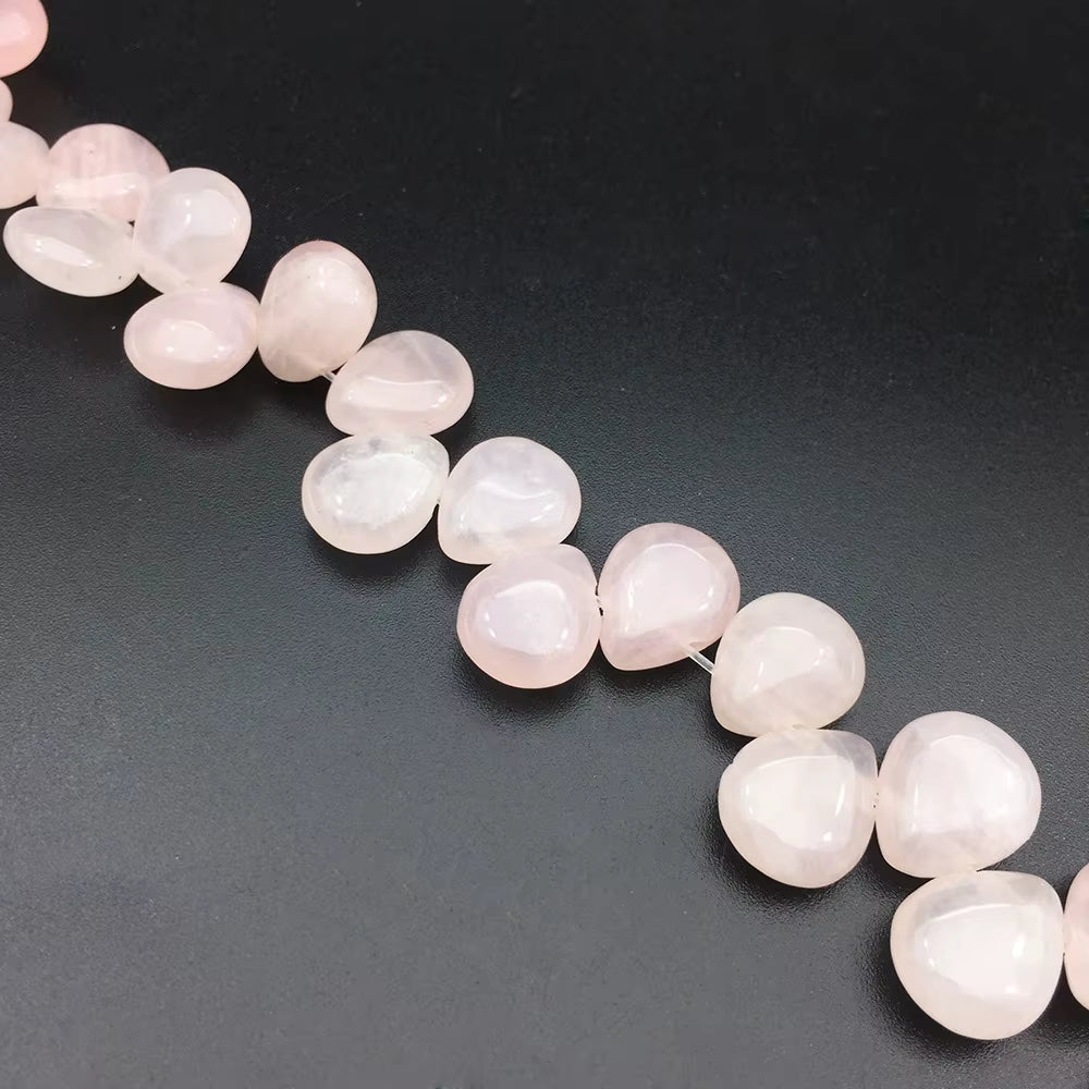 A strand of polished rose quartz gemstone beads in a teardrop shape, arranged diagonally on a dark gray background.
