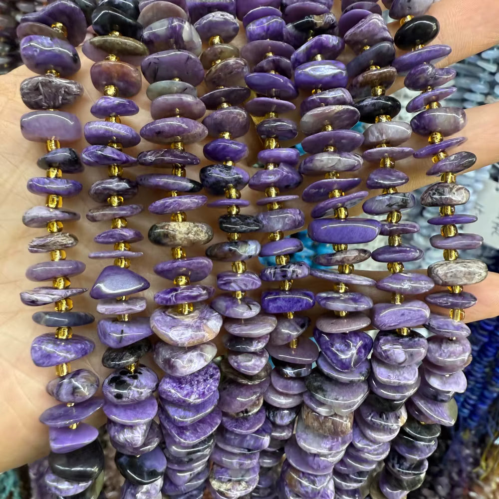 Multiple strands of polished purple stone beads with small gold spacer accents, held in a hand against a blurred background.