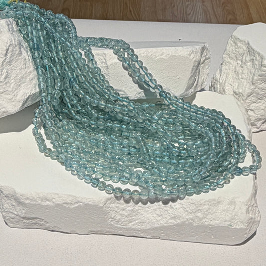 Multiple strands of light blue faceted gemstone beads draped over white textured stone blocks.