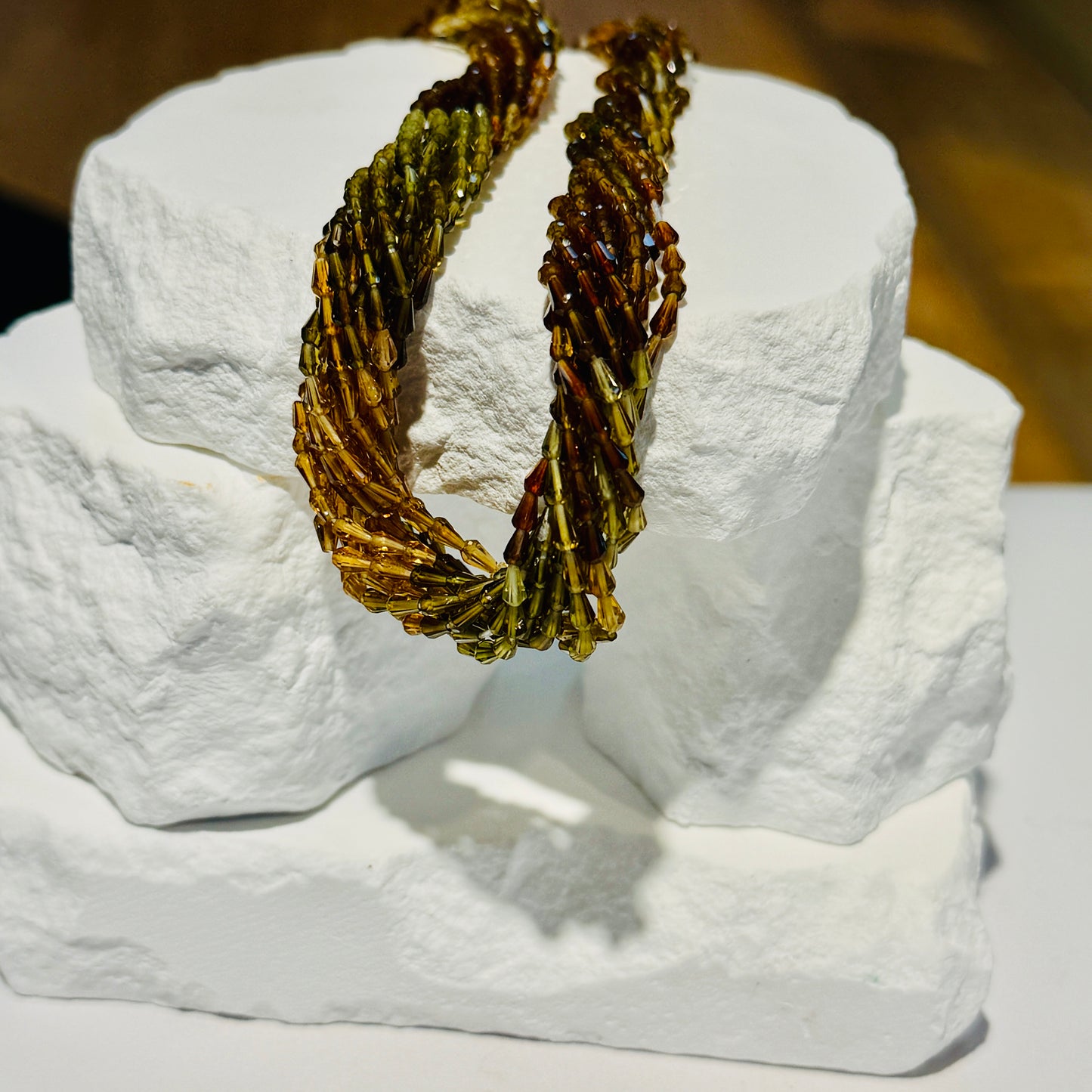 Multi Color Tourmaline beads that are vase shaped and faceted draped over a white rocky background