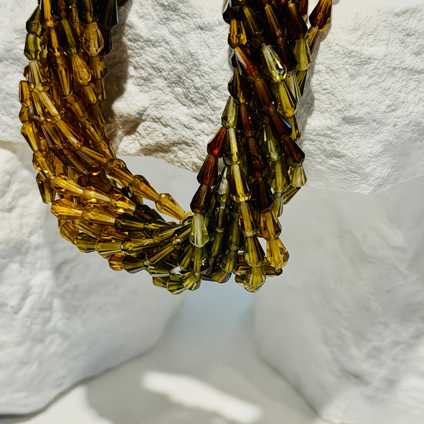 Multi Color Tourmaline beads that are vase shaped and faceted draped over a white rocky background