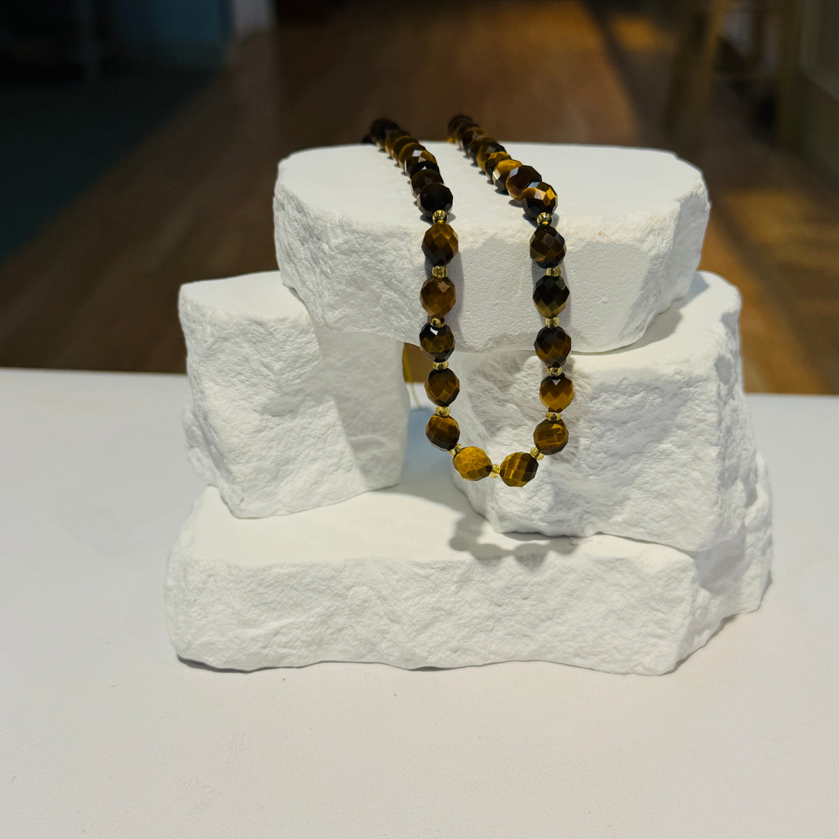 A Strand of faceted  tiger's eye beads in brown and golden-yellow tones, draped over a white stone display stand.