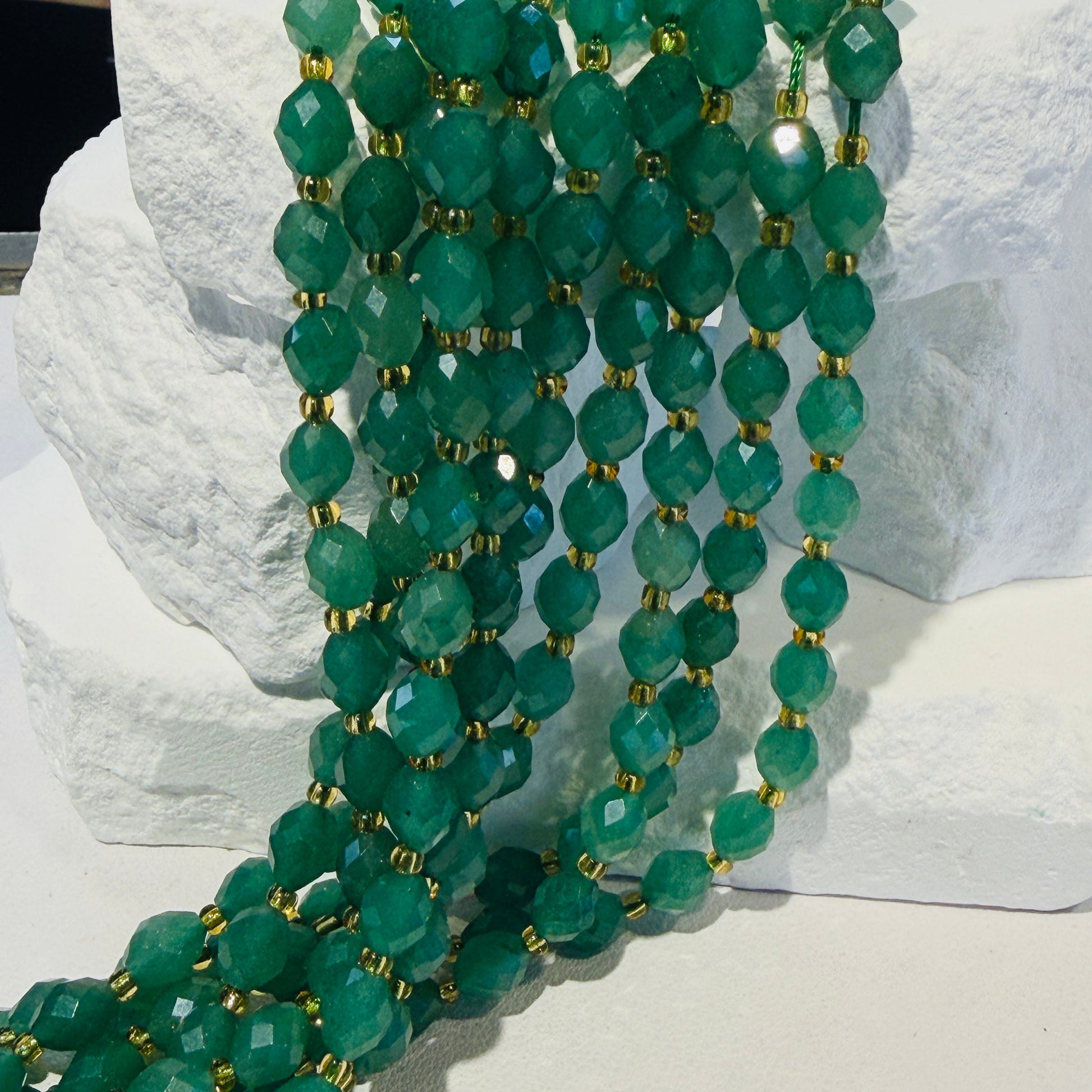 Multiple strands of faceted green Aventurine gemstone beads separated by small gold spacer beads, draped over a white stone display block.