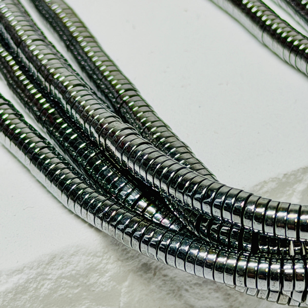 A close-up of several metallic silver Flat Roundel Beads draped across a white surface.