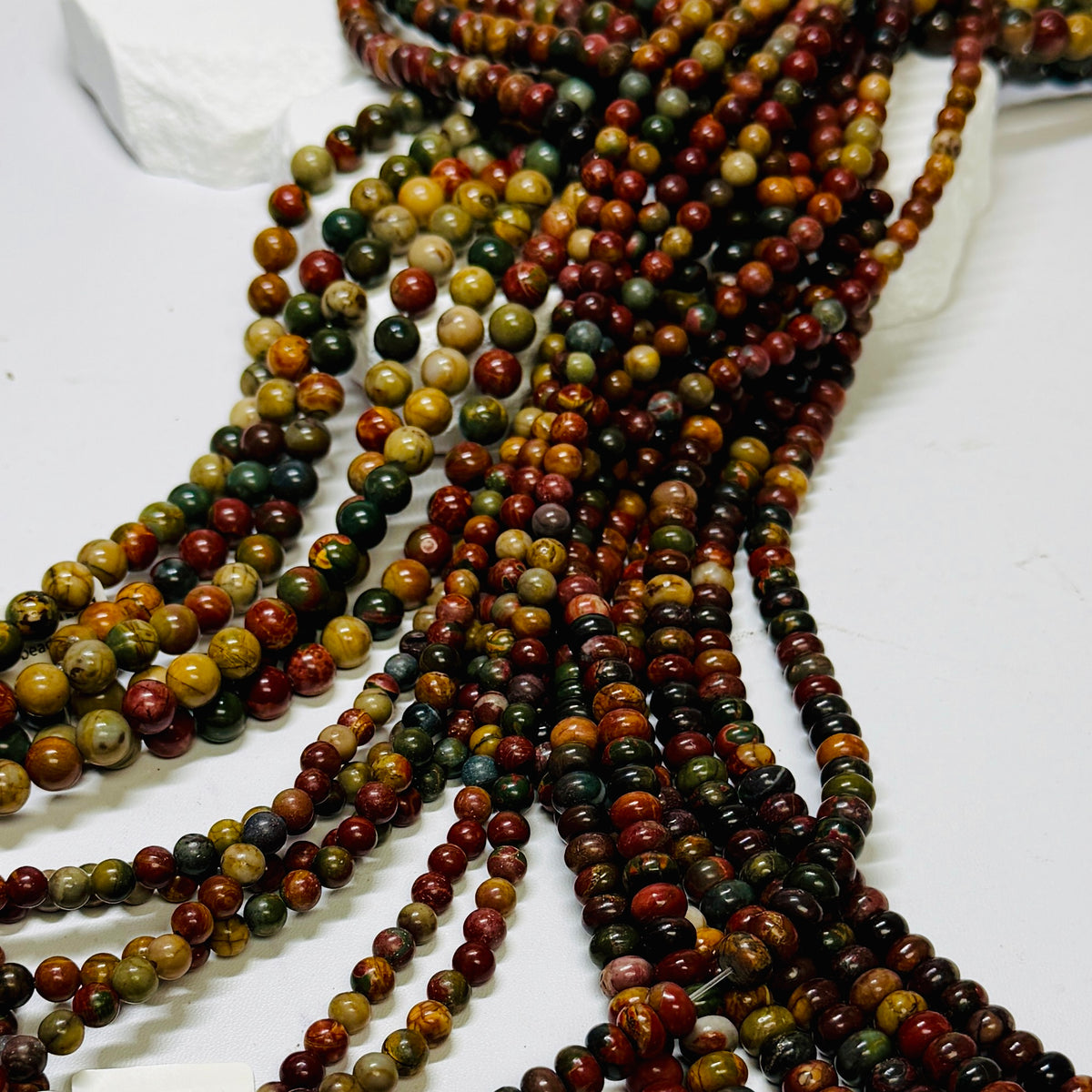 Strands of Picasso stones, round and roundel, over a white display