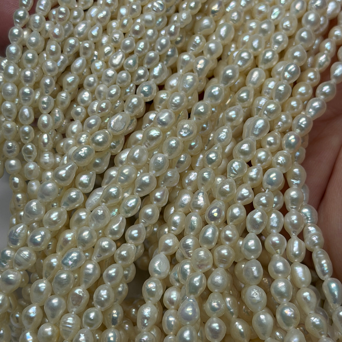 Close-up of multiple strands of irregular drop white freshwater pearls held in a hand, showing their lustrous, glossy texture.